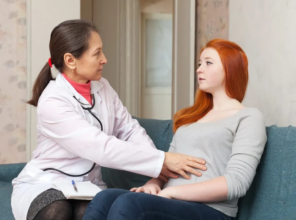 physician touches belly of teenager girl in interior. Focus on patient