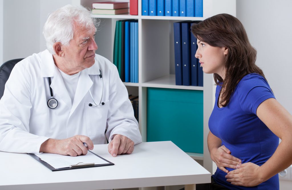 Young woman with stomachache visiting senior doctor